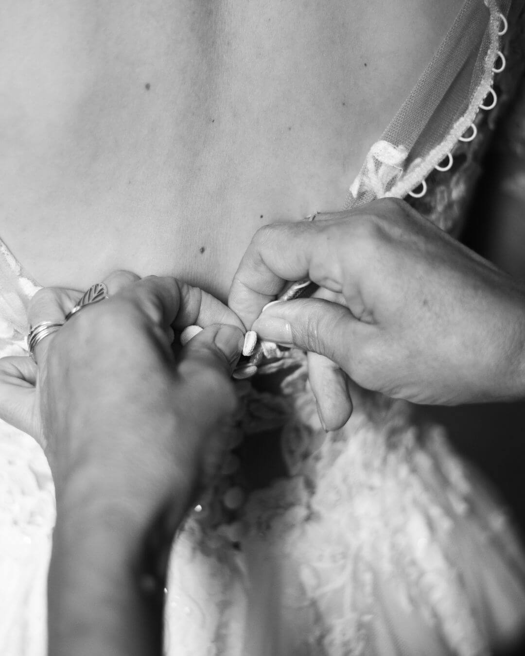 Gros plan de la mariée en train d'enfiler sa robe en noir et blanc